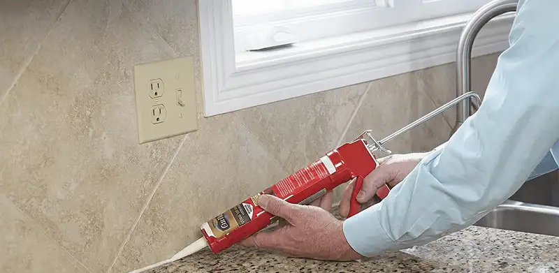 Handyman applying caulk along a kitchen backsplash and countertop seam in Bakersfield, CA