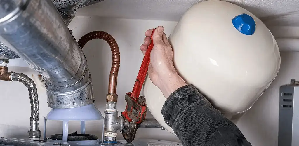 Water heater repair technician tightening plumbing connections near a tank unit in Bakersfield, CA